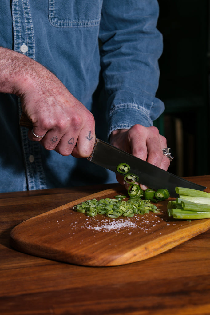 man's hands cutting chives with a Bayali Uzbek handmade kitchen knife and a senegalese chopping board